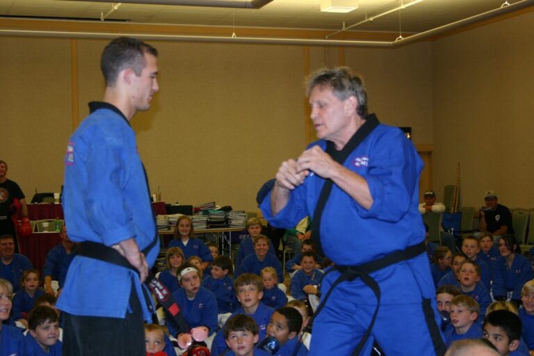 Two Black Belts in blue uniforms demonstrating in front of seated students at the 2007 Champion's Reunion