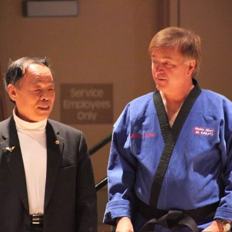 Grand Master Jhoon Rhee in a dark suit beside Stephen Oliver, whose blue uniform is embroidered Master Oliver, at the Mile High Karate Black Belt Retreat